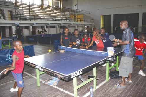 Ganiyu Quadri (left) returns a serve to his coach, who is also his dad, Mr. Quadri (r) while other table tennis players look on during a training session at the camp of Adopt-A-Talent Sports Programme at the UNILAG Sports Centre, Yaba, Lagos, Nigeria. Photo: Akin Farinto.