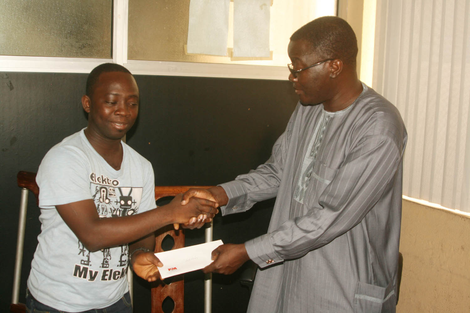 Adegbenle Adedapo (left) receives his $250 cash prize from the Executive Editor of P.M.News, Mr. Kunle Ajibade