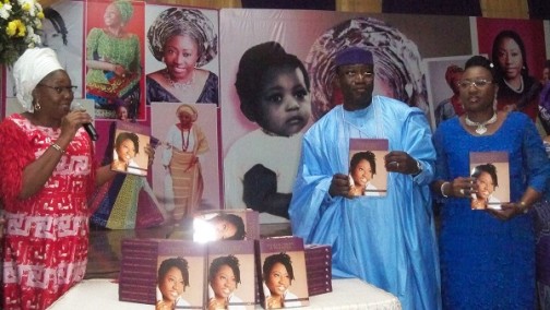 Dame Abimbola Fashola unveils one of the books. Governor Fayemi and his wife stand on the right