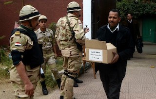 A man carries a box full of voting ballots near Egyptian soldiers today