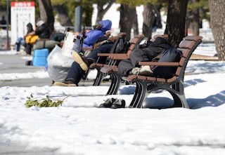 Homeless men take naps on benches at a park in Tokyo on February 16, 2014 after a snow storm hit Japan. Two people were killed when a fresh snow storm hit Japan, disrupting rail and road travel, grounding more than 100 flights. AFP