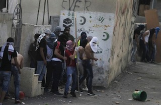 Palestinian youth take cover behind a wall as they hurl stones at Israeli policemen during the protest