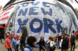 People walk past the work of artist  Mr. Brainwash as he creates a massive 9/11 Mural on the side of Century 21 