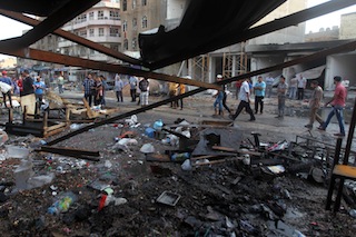 FILE PHOTO: Iraqis stand at the scene of the aftermath of a car bomb in Baghdad