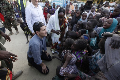 Former UK Foreign Secretary David Miliband, centre, kneels as he listens to children singing "ABC" displace by Boko haram attacks, in a camp in Maiduguri, Nigeria,  Monday, Dec. 7, 2015, in the heart of Nigerias war zone.  Miliband, now president of the International Rescue Committee, dropped to kneel to make eye contact with children in a refugee camp Maiduguri, the northeastern city that has 1 million residents and 2 million refugees, half of them children. (AP Photo/Sunday Alamba)