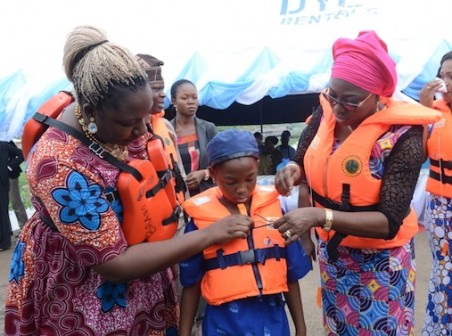 Wife of Lagos State Governor, Mrs. Bolanle Ambode (right) with Managing Director, Lagos State Waterways Authority (LASWA), Ms. Abisola Kamson (left), jointly wearing a life jacket on a student, during the distribution of Life Jackets to students and pupils in Epe Local Government as part of Campaign of Water Transport Safety Awareness Programme, organized by LASWA in partnership with Total Nigeria Limited, on Wednesday, February 17, 2016