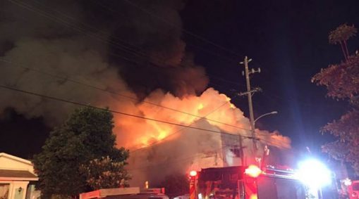 Flames rise from the top of a warehouse, which caught fire during a dance party in Oakland