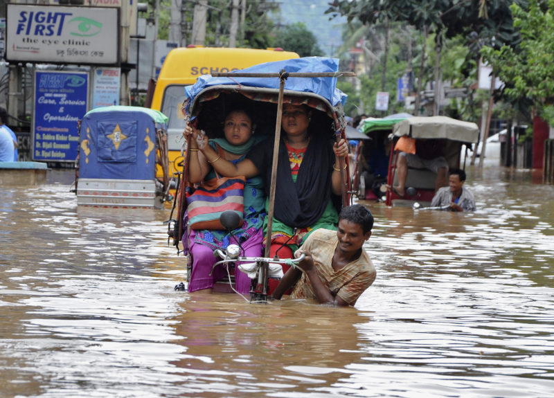 People use cycle rickshaws to commute through a flooded road after heavy rains in Guwahati