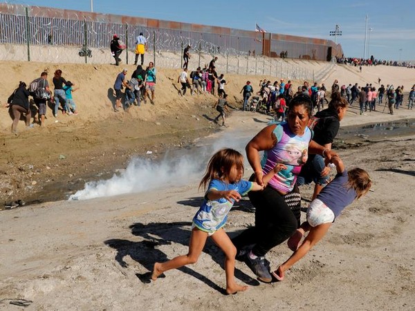 A migrant family runs away from tear gas in front of the border wall between the U.S and Mexico, in Tijuana