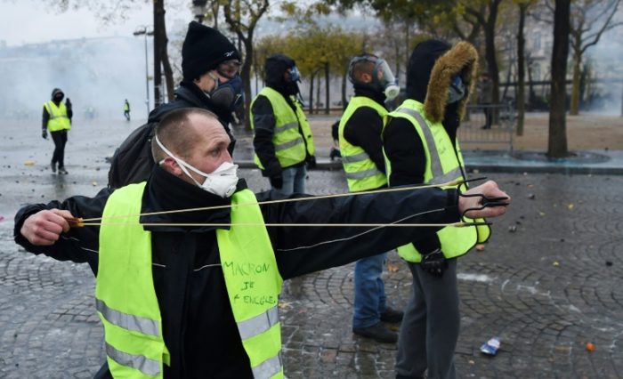 A-protesters-aims-a-sling-shot-against-a-Parisian-police-e1543666793101