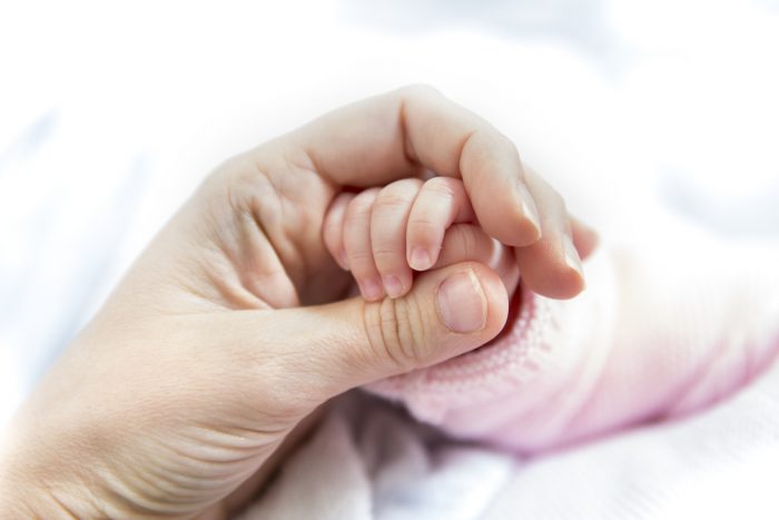 Mother’s hand holding newborn baby’s hand