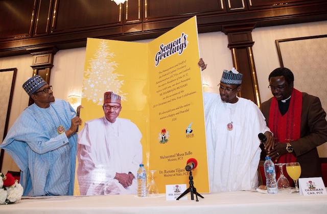 Buhari looks up the ceiling wards to read the card’s content. Right is Muhammad Musa Bello, FCT Minister and Malomo