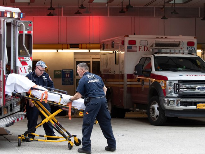 New York parademics place an empty collapsible wheeled stretcher into an ambulance