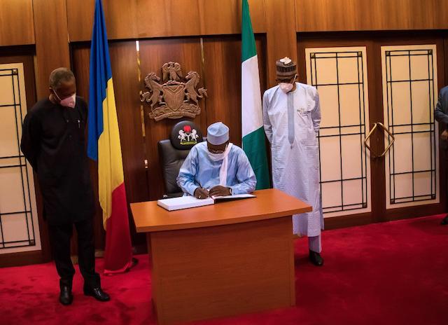 Deby signing the visitors register for the last time. Left is Nigeria's foreign minister Geoffrey Onyeama