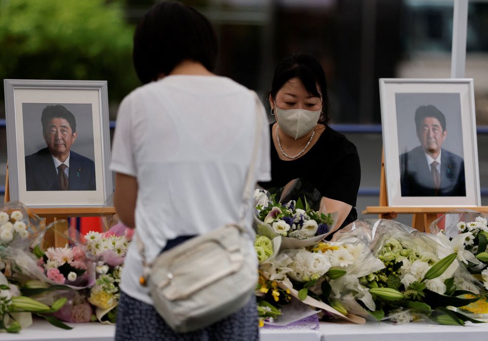 A mourner offers flowers next to pictures of late former Japanese Prime Minister Shinzo Abe, who was shot while campaigning for a parliamentary election, on the day to mark a week after his assassination at the Liberal Democratic Party headquarters in Tokyo, Japan July 15, 2022. REUTERS/Issei Kato