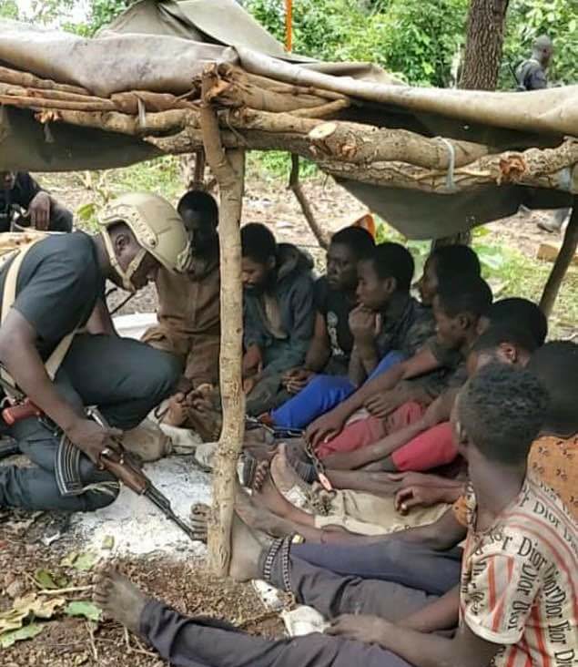 A soldier with the 10 hostages chained and bound with ropes like wild animals discovered during clearance operations in Chikun and Igabi LGs of Kaduna State