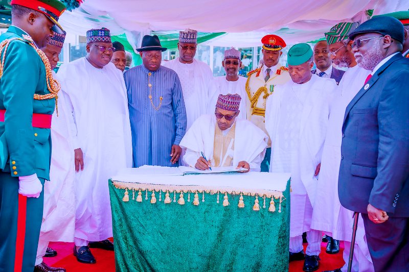 The president signing the anniversary register, with Jonathan and others surrounding him.