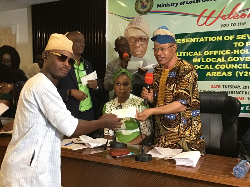 Robert handing over cheque to one of the beneficiaries, while the PS, Bolarinwa looks on.