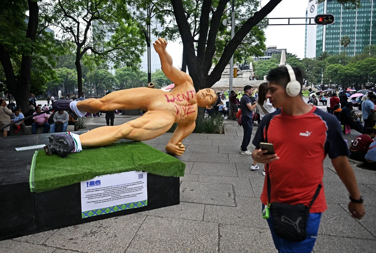 A passer-by walks past a giant sculpture, part of the urban exhibition "Gigantes del Futbol" (Giants of football) which was pulled down during a protest by the National Coordination of Education Workers (CNTE) calling for a general strike and protests around stadiums hosting World Cup matches, ahead of the upcoming FIFA 2026 World Cup, in Mexico City, on June 2, 2026. (Photo by CARL DE SOUZA / AFP)